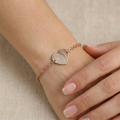 Rose gold bracelet with a heart-shaped charm on a wrist against a beige background