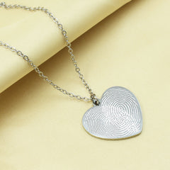Silver heart-shaped fingerprint pendant on a chain against a beige background