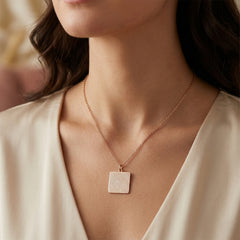 Necklace with a square pendant worn by a person in a beige top