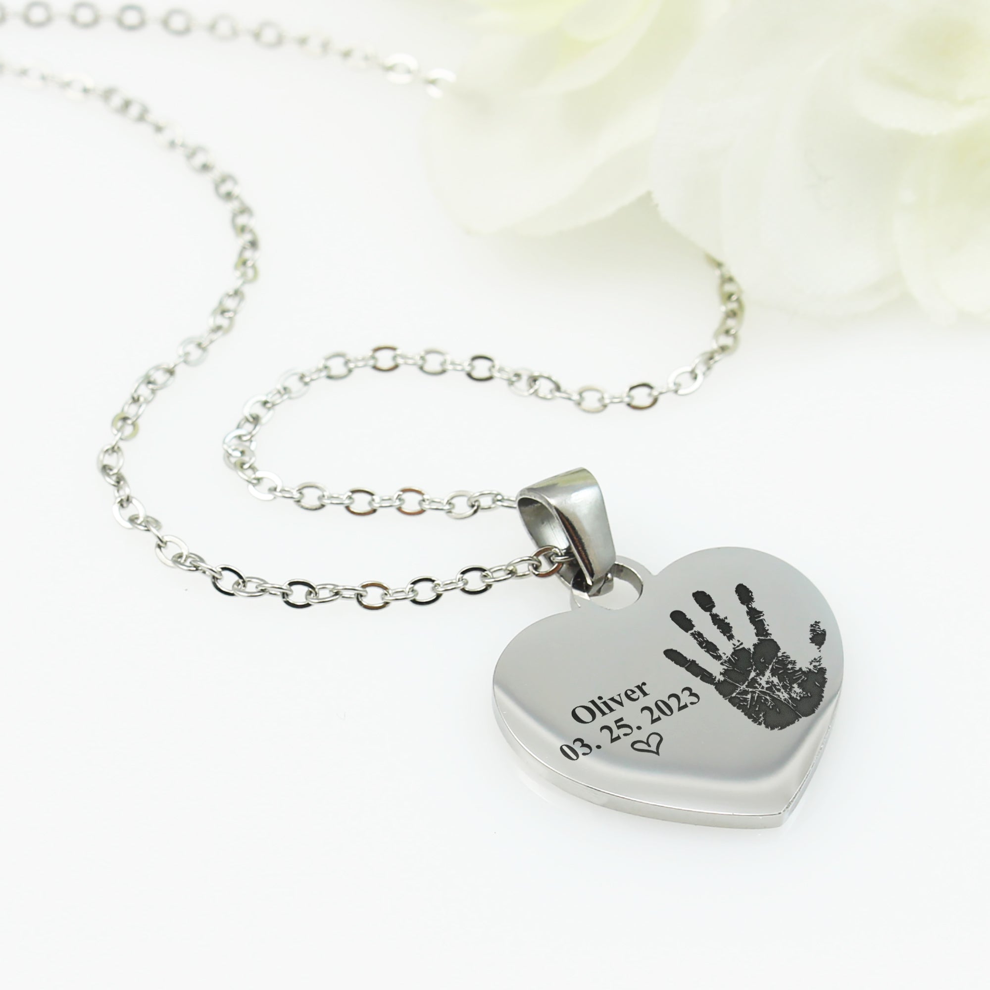 Heart-shaped silver pendant with handprint and engraved text on a white background
