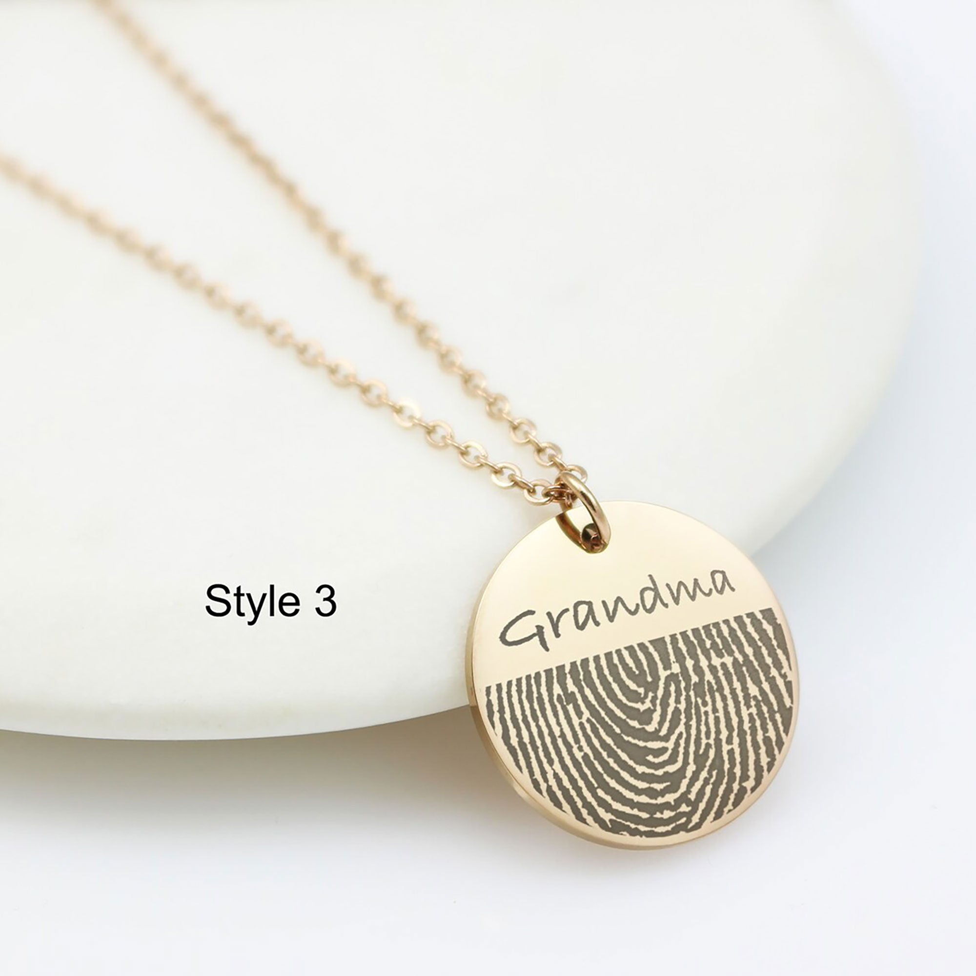 The round disc necklaces in rose gold finishes. The pendant features a high-detail fingerprint engraving. The rose gold discs also include custom name engravings—'Mom' and 'Grandma'—in a delicate cursive script.