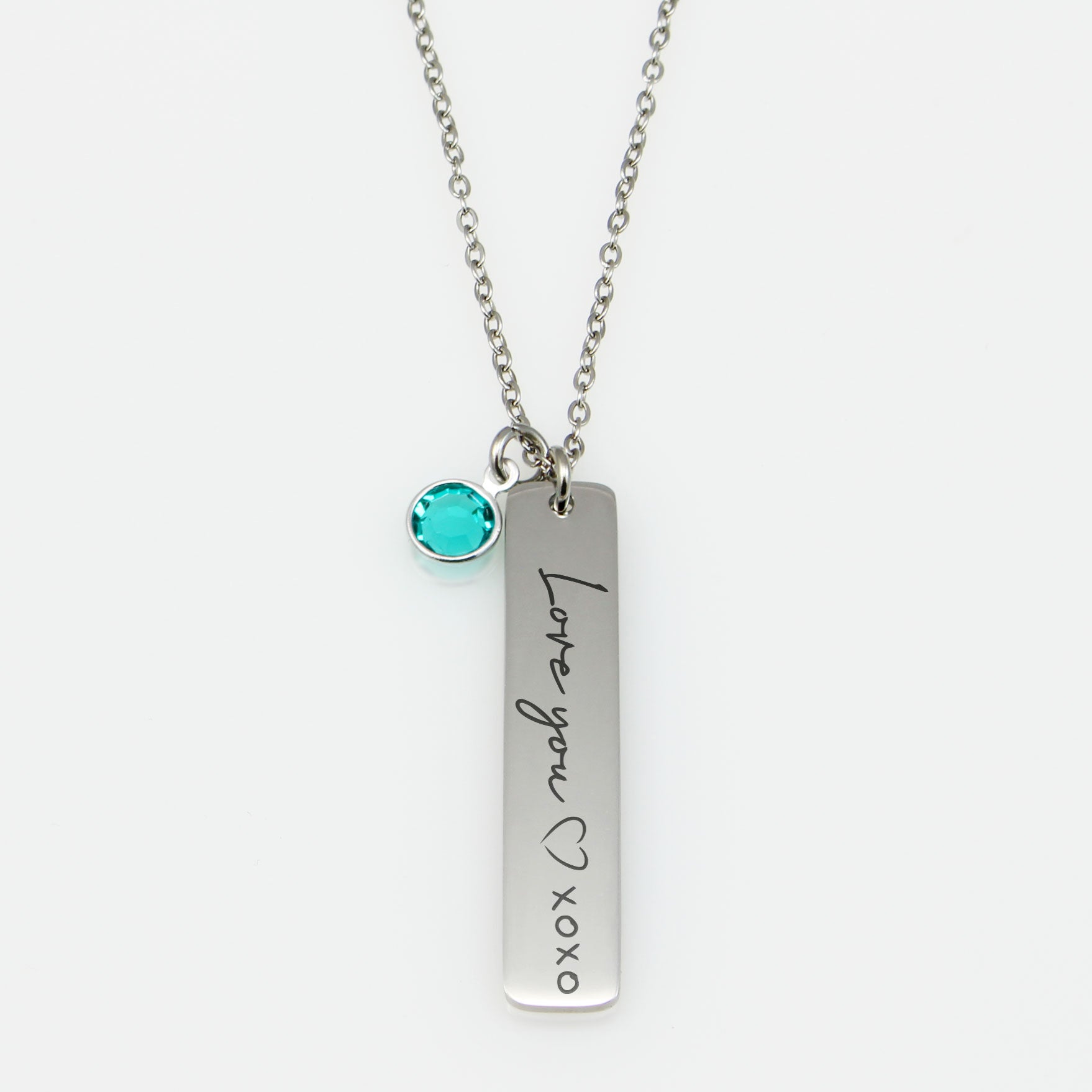 "Personalized birthstone bar jewelry: vertical metal tags engraved with names in cursive, featuring a solitary colorful crystal accent. Available for multiple family members, shown in silver."