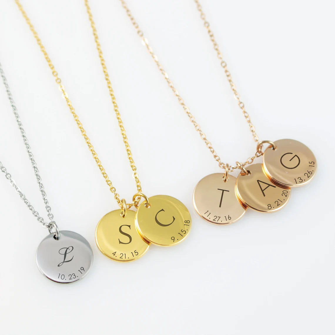 Three necklaces with stainless steel pendants. From left to right, the pendants are gold, silver, and rose gold, each engraved with different initials and birthdates.