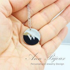 Silver necklace with a round pendant featuring the letter 'W' held in a hand, branded 'Ann Bijoux'.