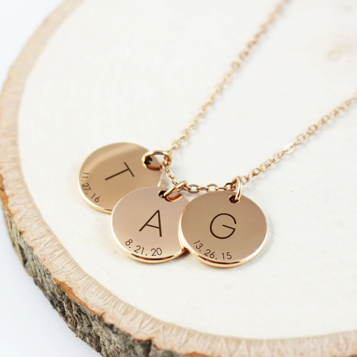 Three necklaces showing different customization options: a single silver disc with a script letter, two gold discs with serif initials, and three rose gold discs, all featuring engraved dates.