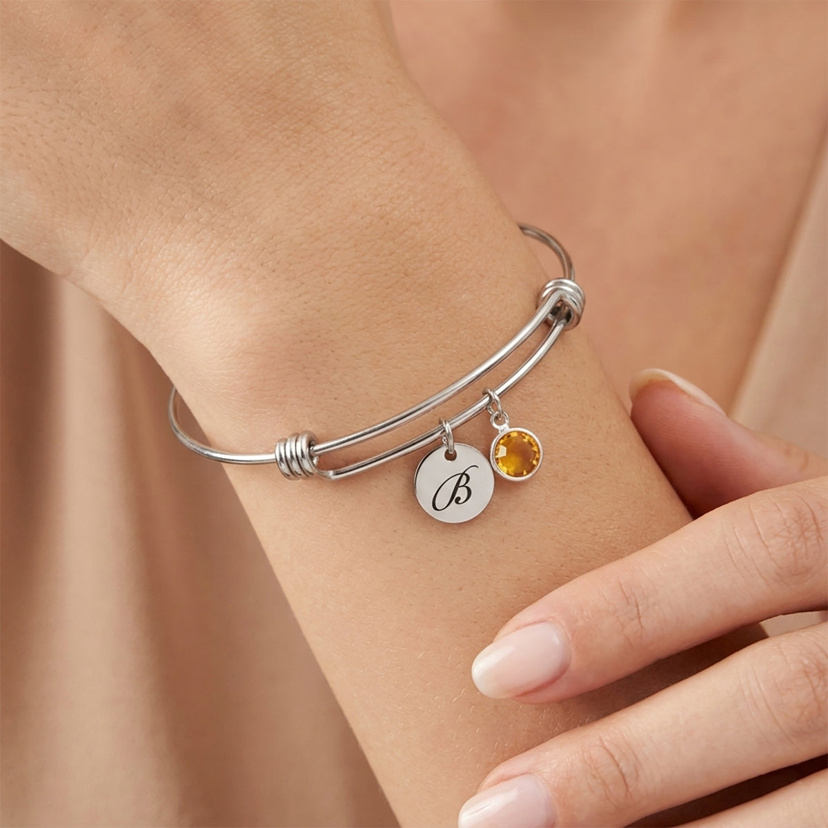 Silver bracelet with a yellow gemstone and round charm on a wrist against a beige background