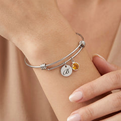 Silver bracelet with a yellow gemstone and round charm on a wrist against a beige background