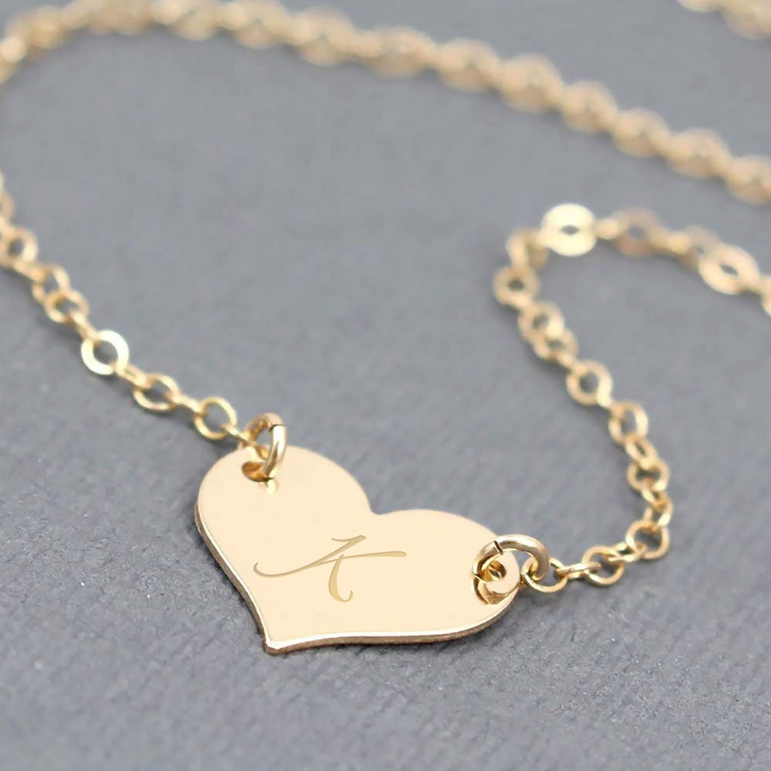Gold heart-shaped necklace with an engraved letter 'A' on a gray background