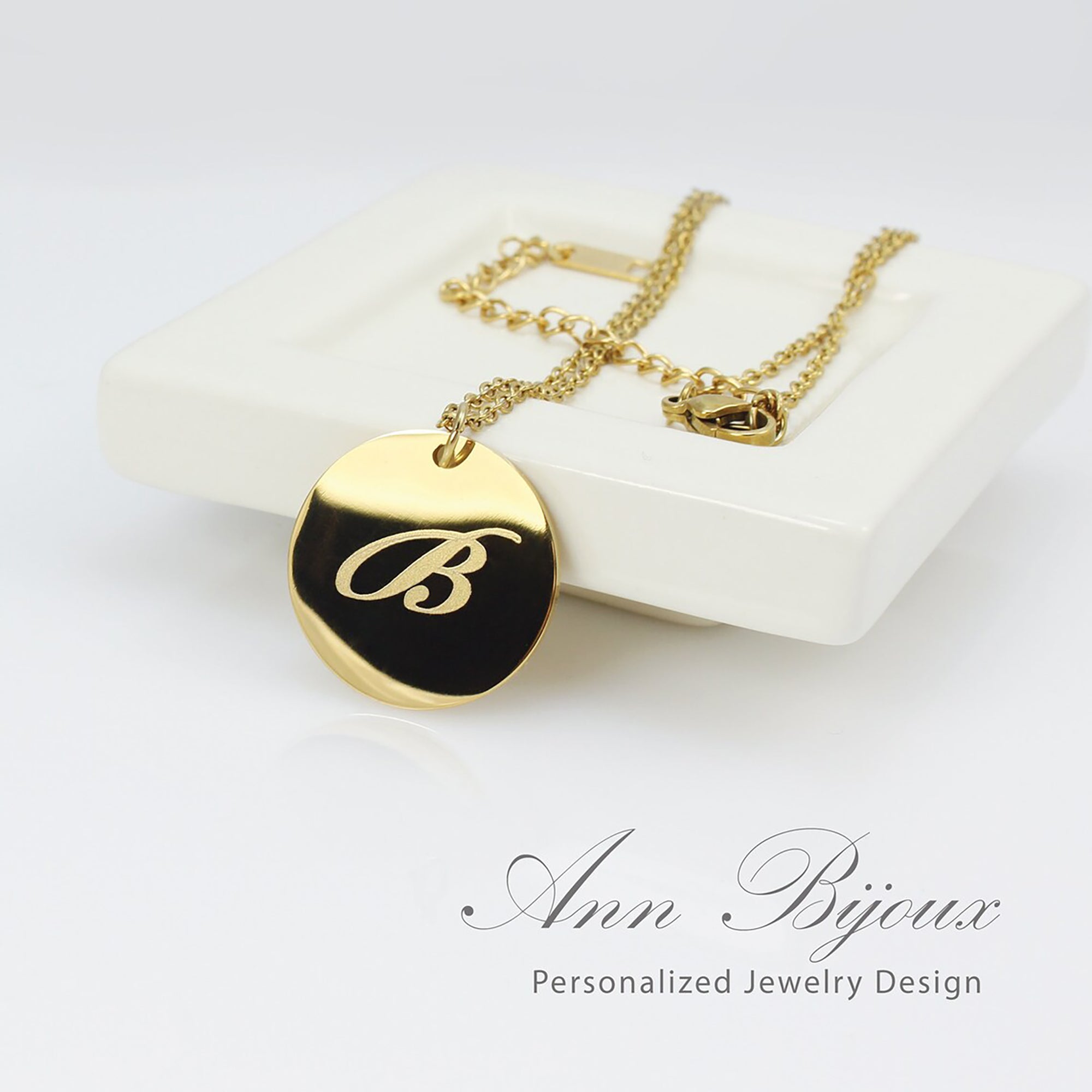 Gold necklace with a black pendant featuring the letter 'B', displayed on a white surface with 'Ann Bijoux' branding.