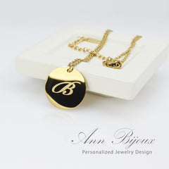 Gold necklace with a black pendant featuring the letter 'B', displayed on a white surface with 'Ann Bijoux' branding.
