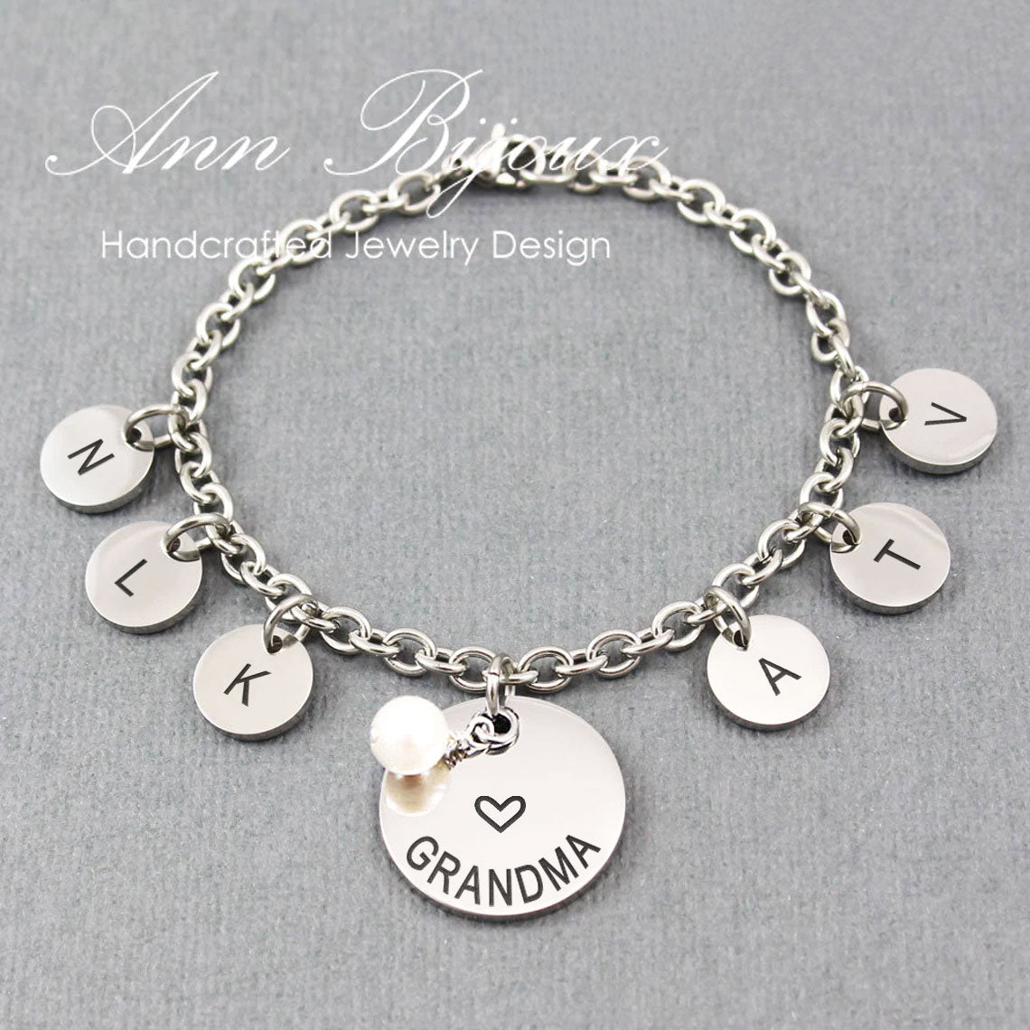 A bracelet with laser engraved stainless steel discs with the letters 'G', 'R', 'A', 'M', 'A' and an engraved heart that reads 'GRANDMA', attached to a stainless steel cable chain with a fresh water pearl.