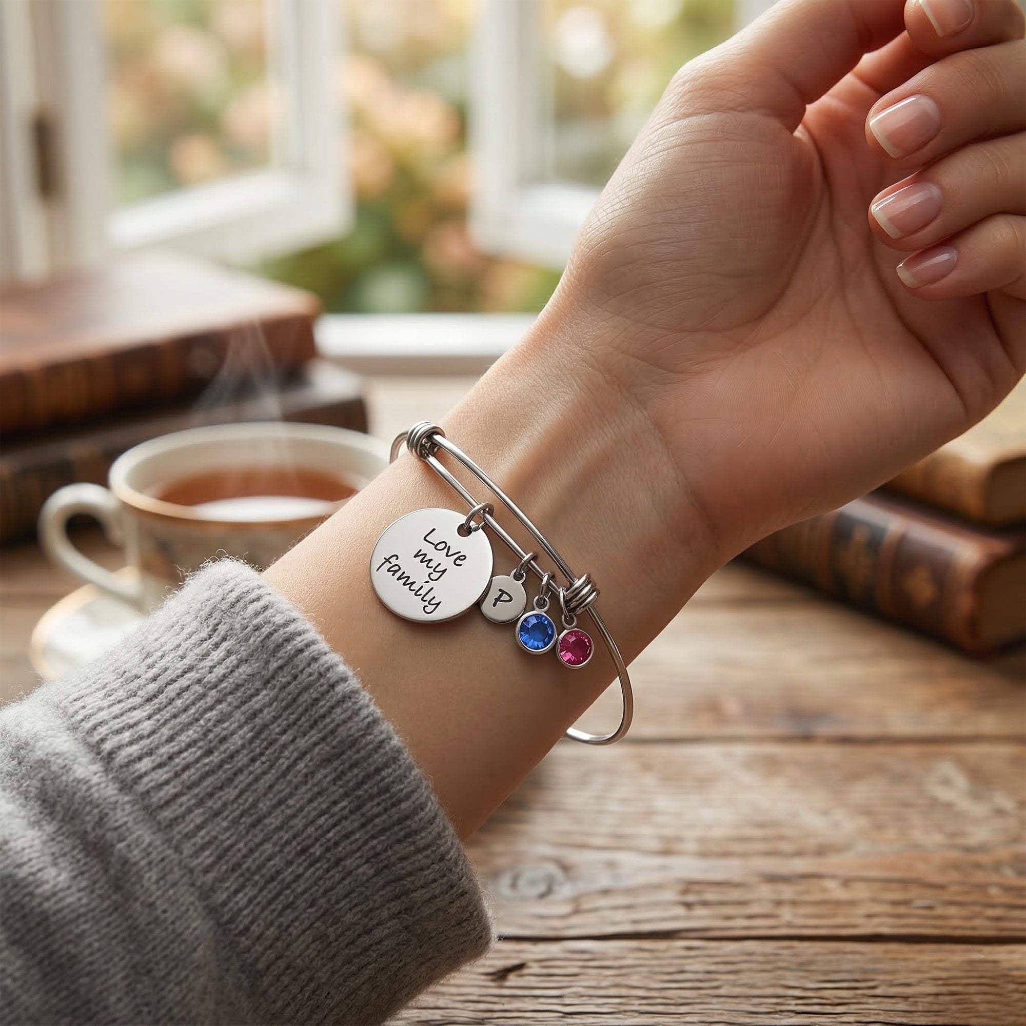 Hand wearing a bracelet with charms on a wooden table with a cup of tea in the background
