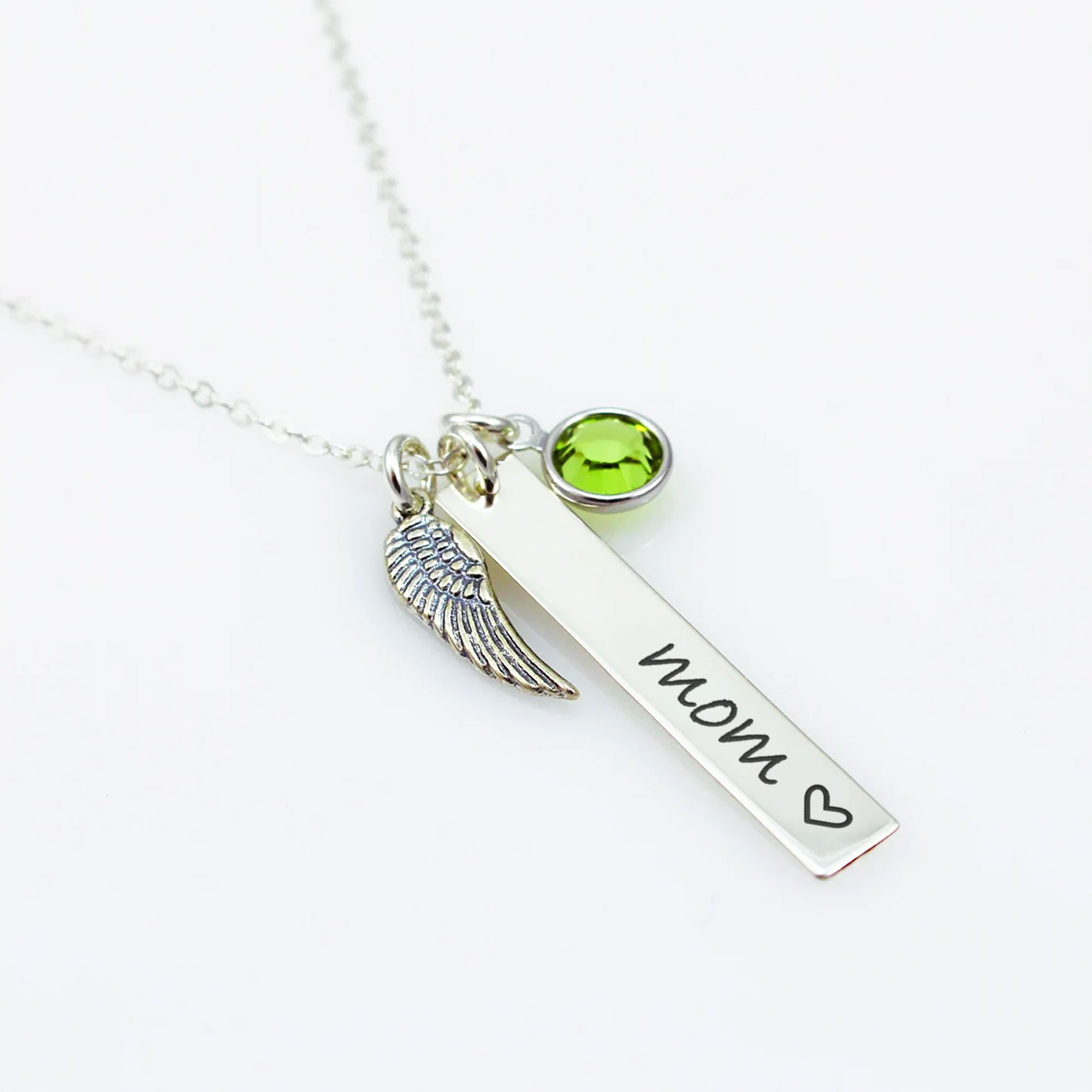 A sterling silver bar necklace with a wing charm and a green Swarovski crystal birthstone, engraved with the word 'Mom' and a heart symbol.