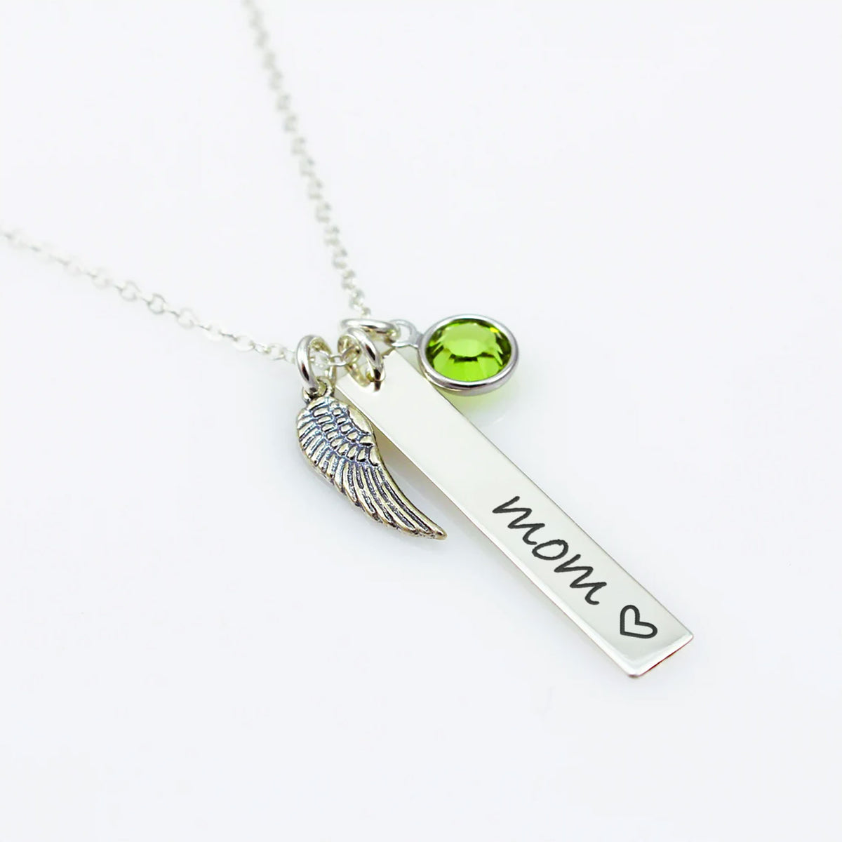 A sterling silver bar necklace with a wing charm and a green Swarovski crystal birthstone, engraved with the word 'Mom' and a heart symbol.