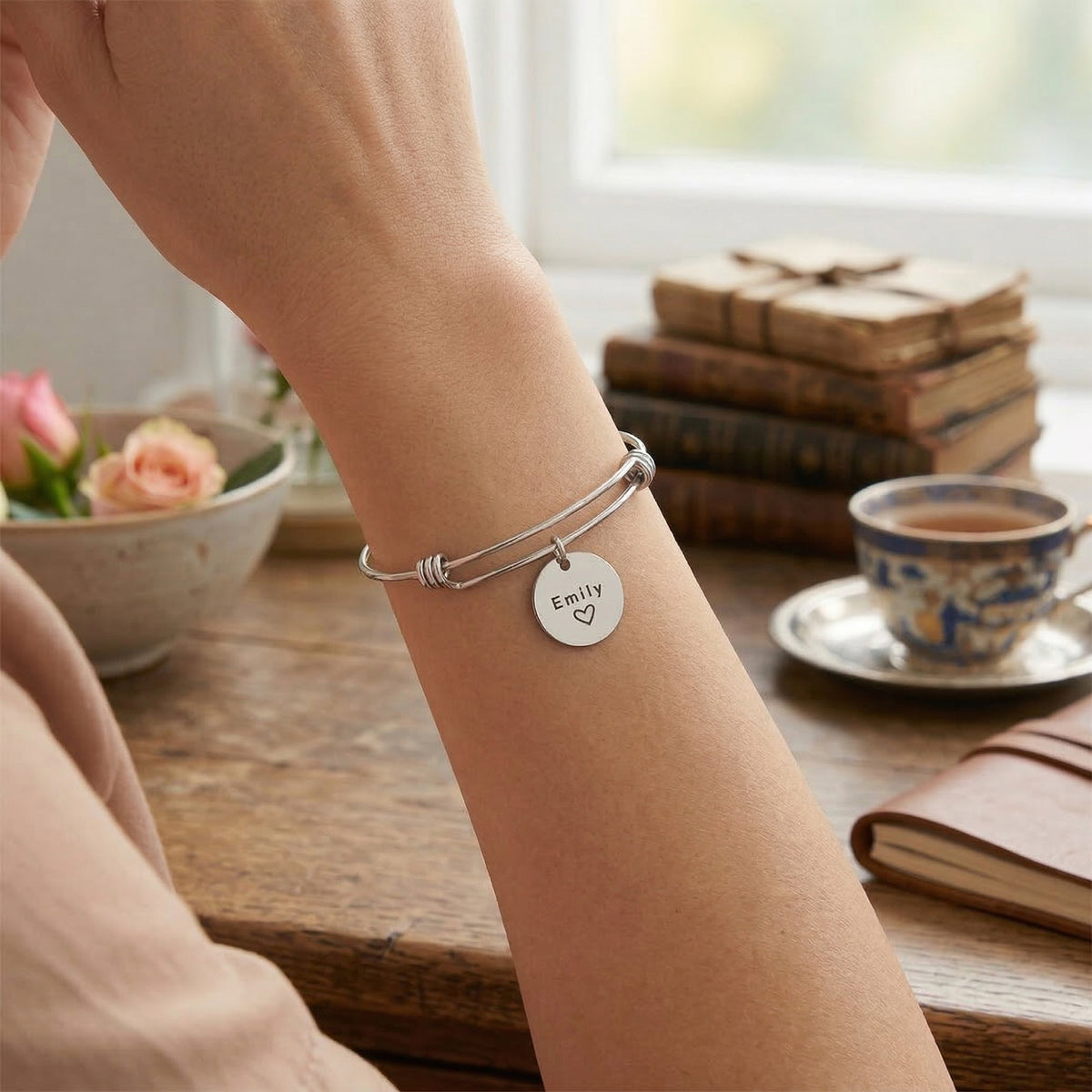 Person wearing a silver bracelet with a name tag on a table with books and a cup of tea.