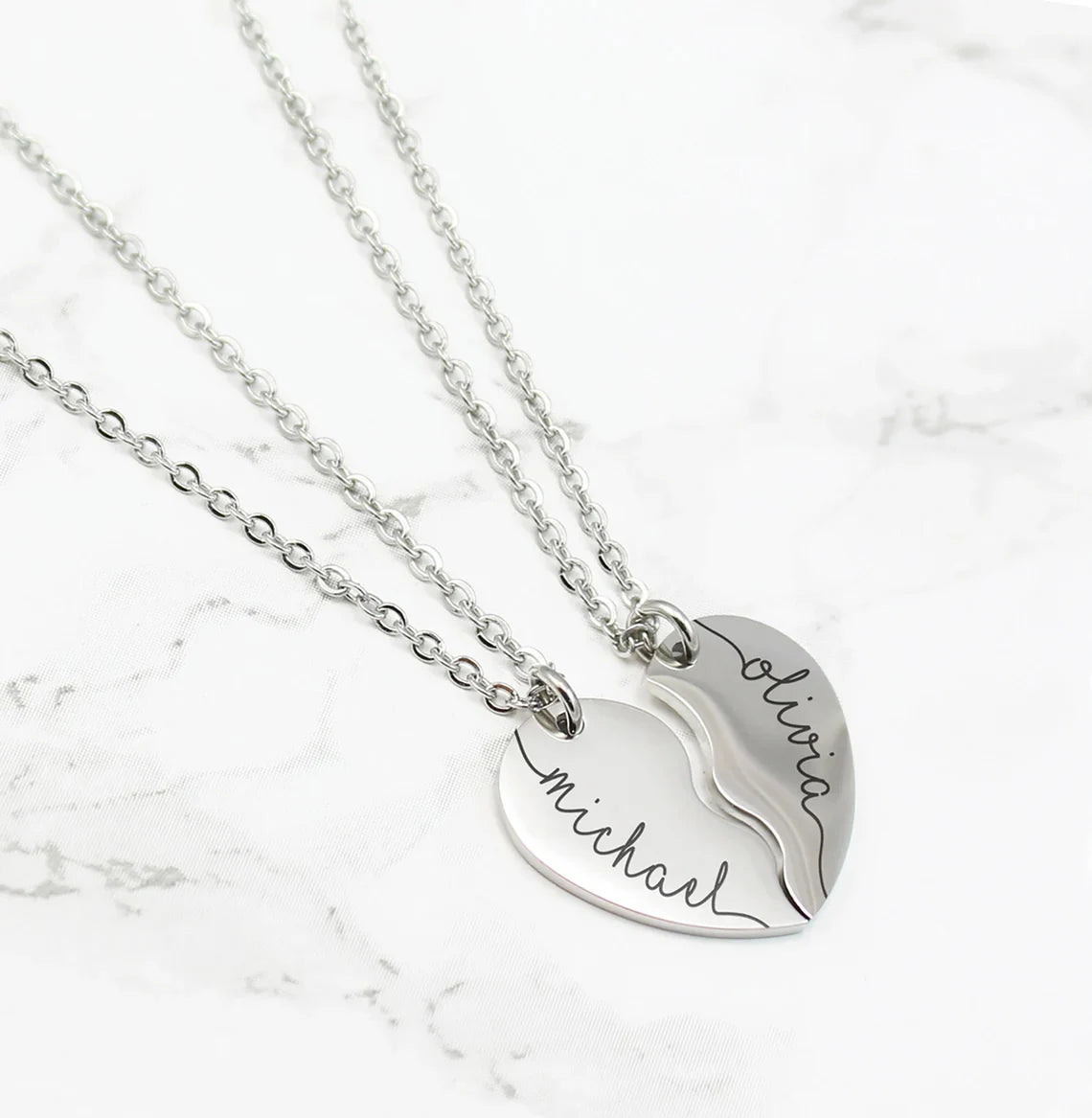 A stainless steel couple heart pendant necklace with the names Michael and Olivia engraved on it, connected by a chain.