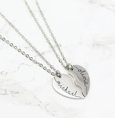 A stainless steel couple heart pendant necklace with the names Michael and Olivia engraved on it, connected by a chain.