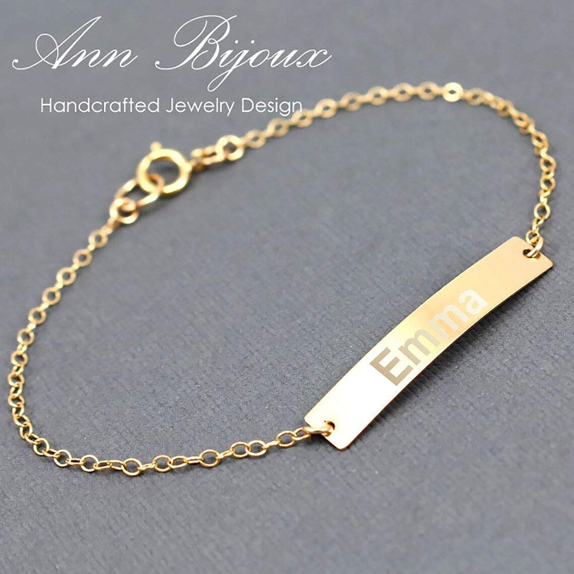 Gold bracelet with engraved name on a gray background, branded 'Ann Bijoux'.