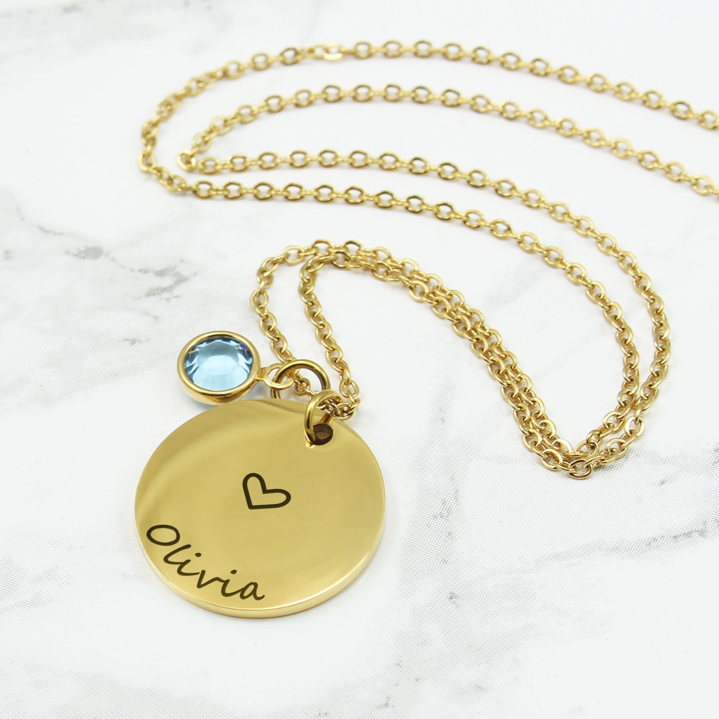 Elegant and minimalist, it features a polished circular pendant delicately engraved with custom names and a sweet heart motif, paired with a sparkling birthstone charm for a pop of meaningful color.