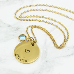 Elegant and minimalist, it features a polished circular pendant delicately engraved with custom names and a sweet heart motif, paired with a sparkling birthstone charm for a pop of meaningful color.