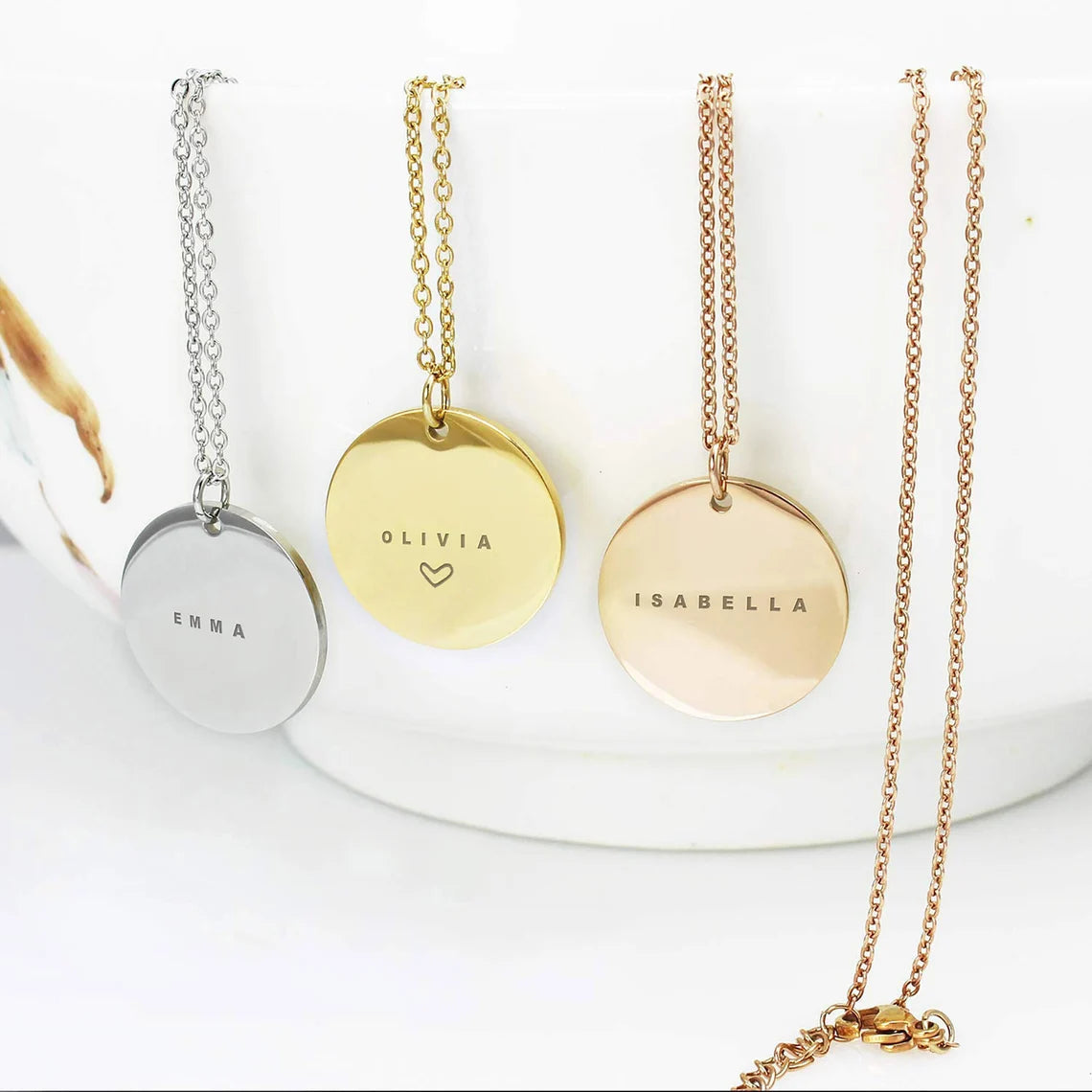 Personalized name necklaces in silver, gold, and rose gold featuring round disc pendants engraved with names Emma, Olivia, and Isabella.