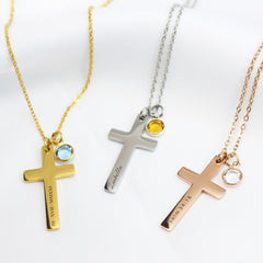Three personalized cross necklaces in gold, silver, and rose gold. Each cross features a different custom engraving—Roman numerals, the name Isabella, and a Bible verse—paired with a small, colorful round birthstone charm.