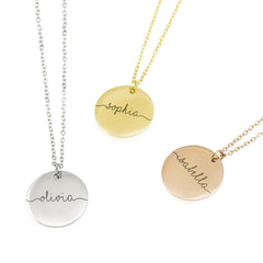 Three round personalized disc necklaces in silver, gold, and rose gold. Each pendant is engraved with a name—Olivia, Sophia, and Isabella—in a flowing, continuous line cursive script that extends to the edges of the disc.