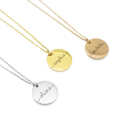 Three round personalized disc necklaces in silver, gold, and rose gold. Each pendant is engraved with a name—Olivia, Sophia, and Isabella—in a flowing, continuous line cursive script that extends to the edges of the disc.