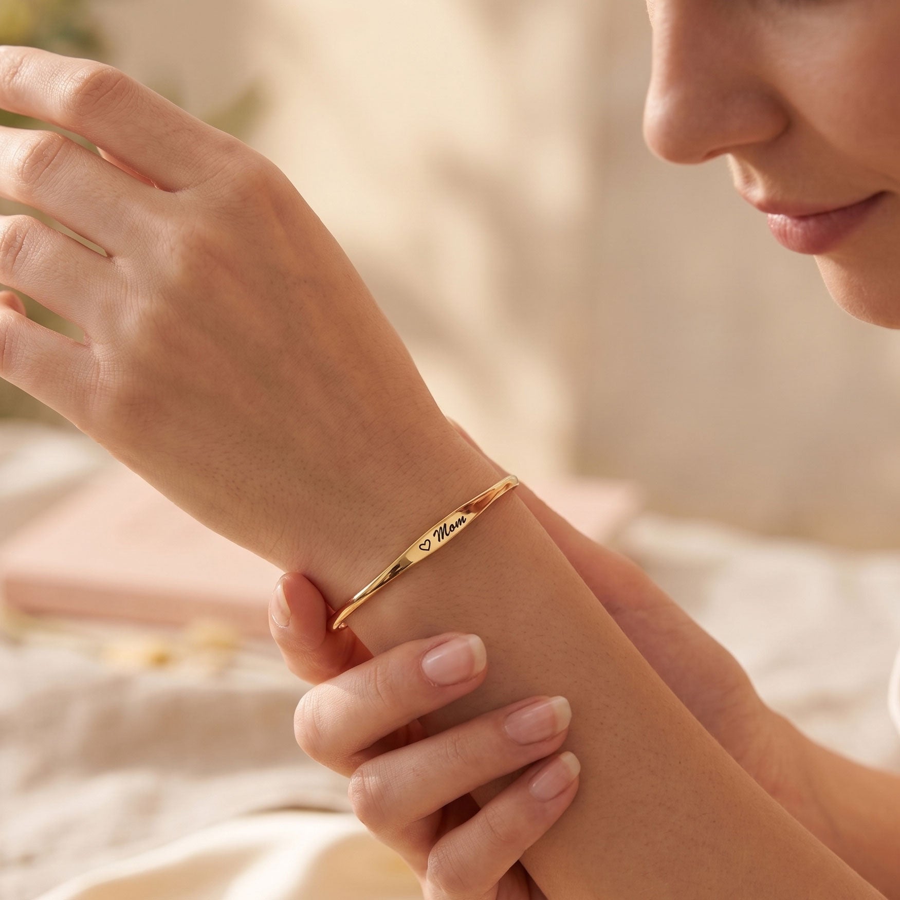 A close-up lifestyle shot of a woman wearing a slim gold bangle bracelet engraved with the name 'Isabel'.