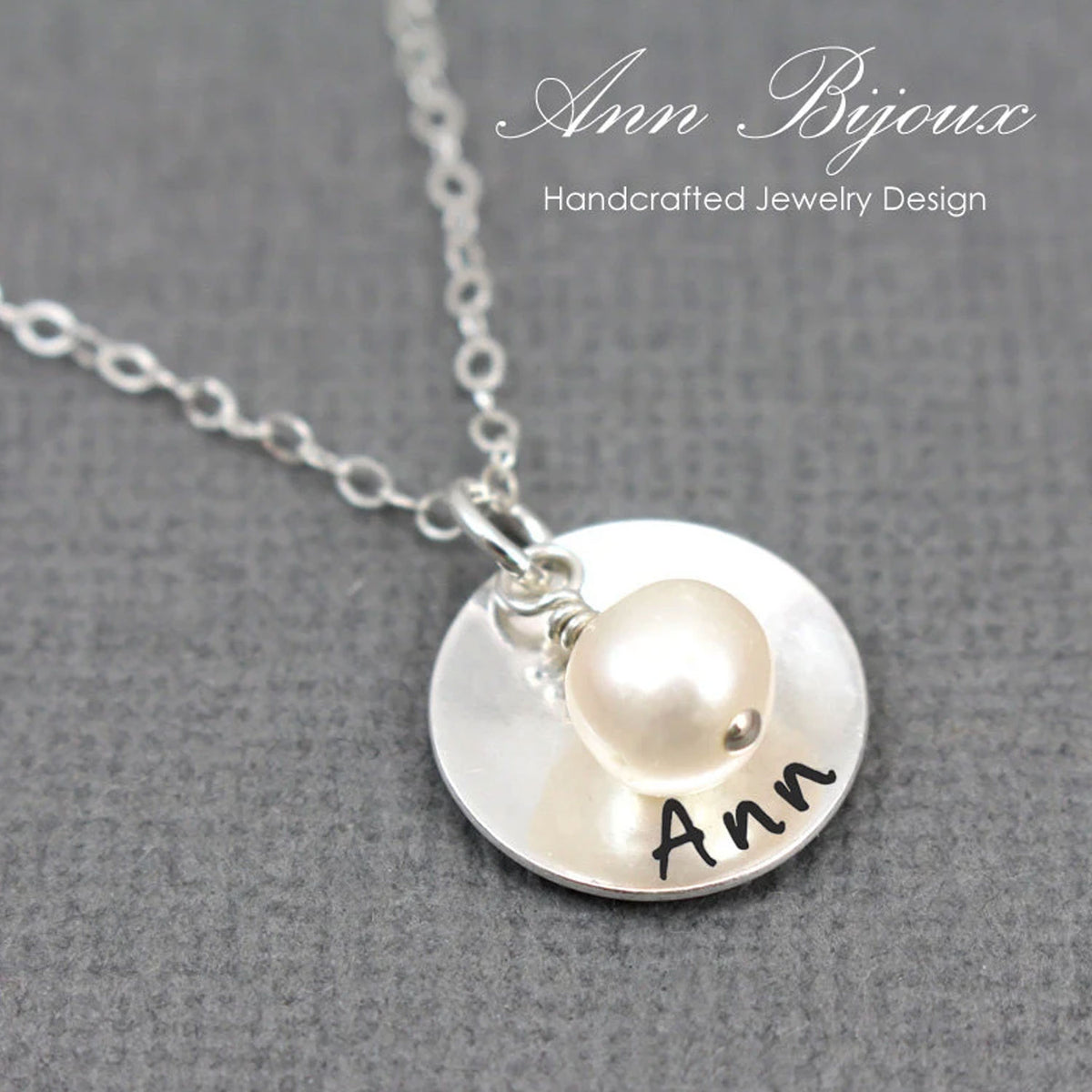 Silver necklace with a round pendant featuring a pearl and engraved name on a gray background.