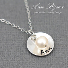 Silver necklace with a round pendant featuring a pearl and engraved name on a gray background.