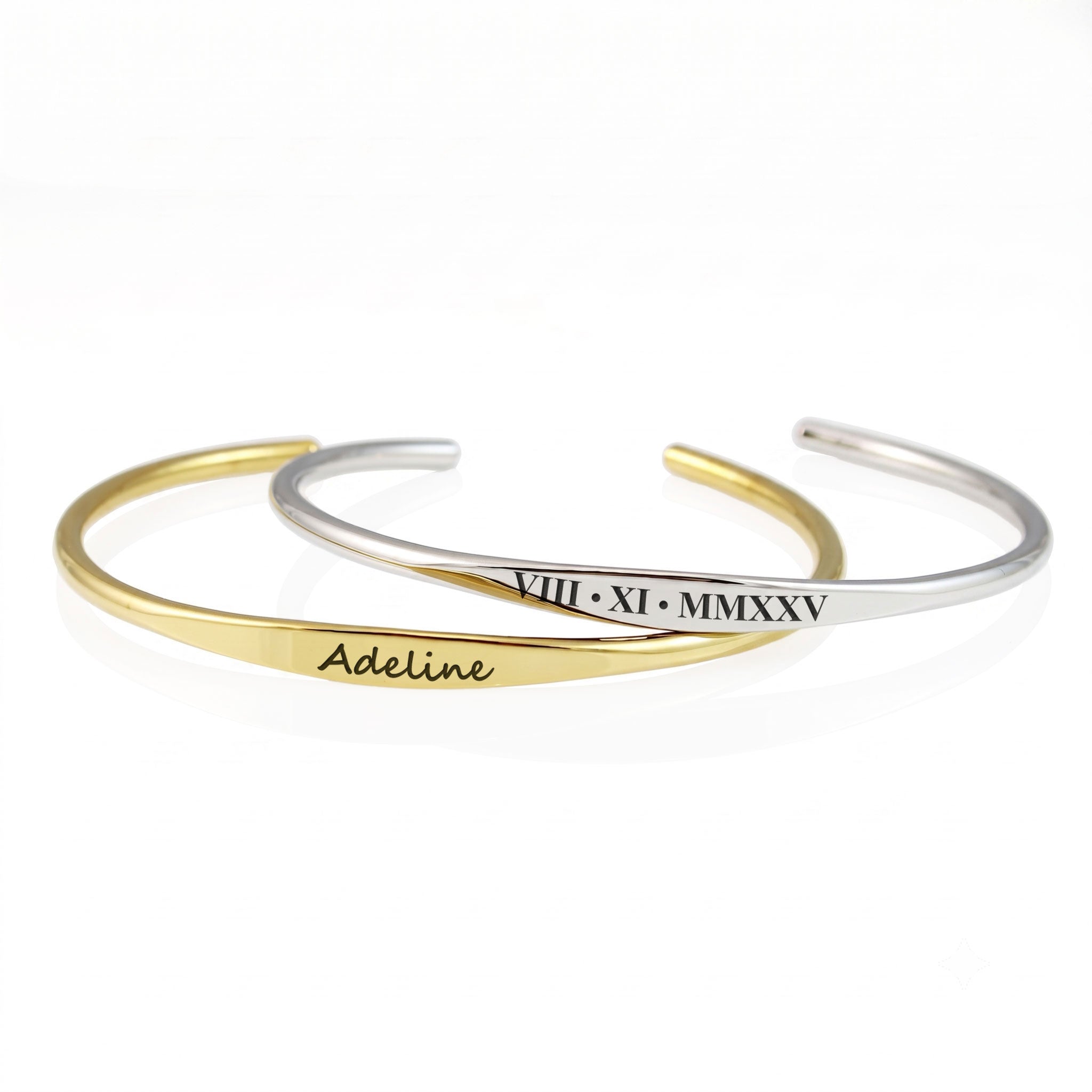 Two slim open cuff bracelets on a white background, one in gold with the name 'Adeline' engraved and the other in silver with Roman numerals engraved.