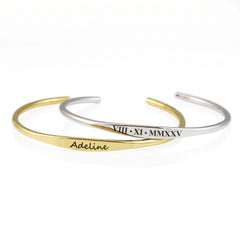 Two slim open cuff bracelets on a white background, one in gold with the name 'Adeline' engraved and the other in silver with Roman numerals engraved.