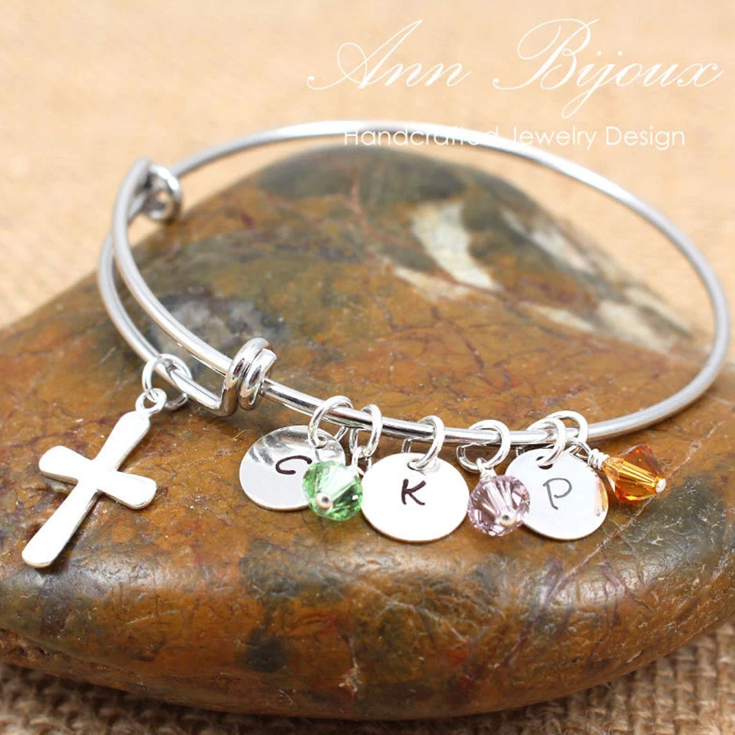 Silver bracelet with charms on a stone surface, featuring the brand 'Ann Bijoux'.