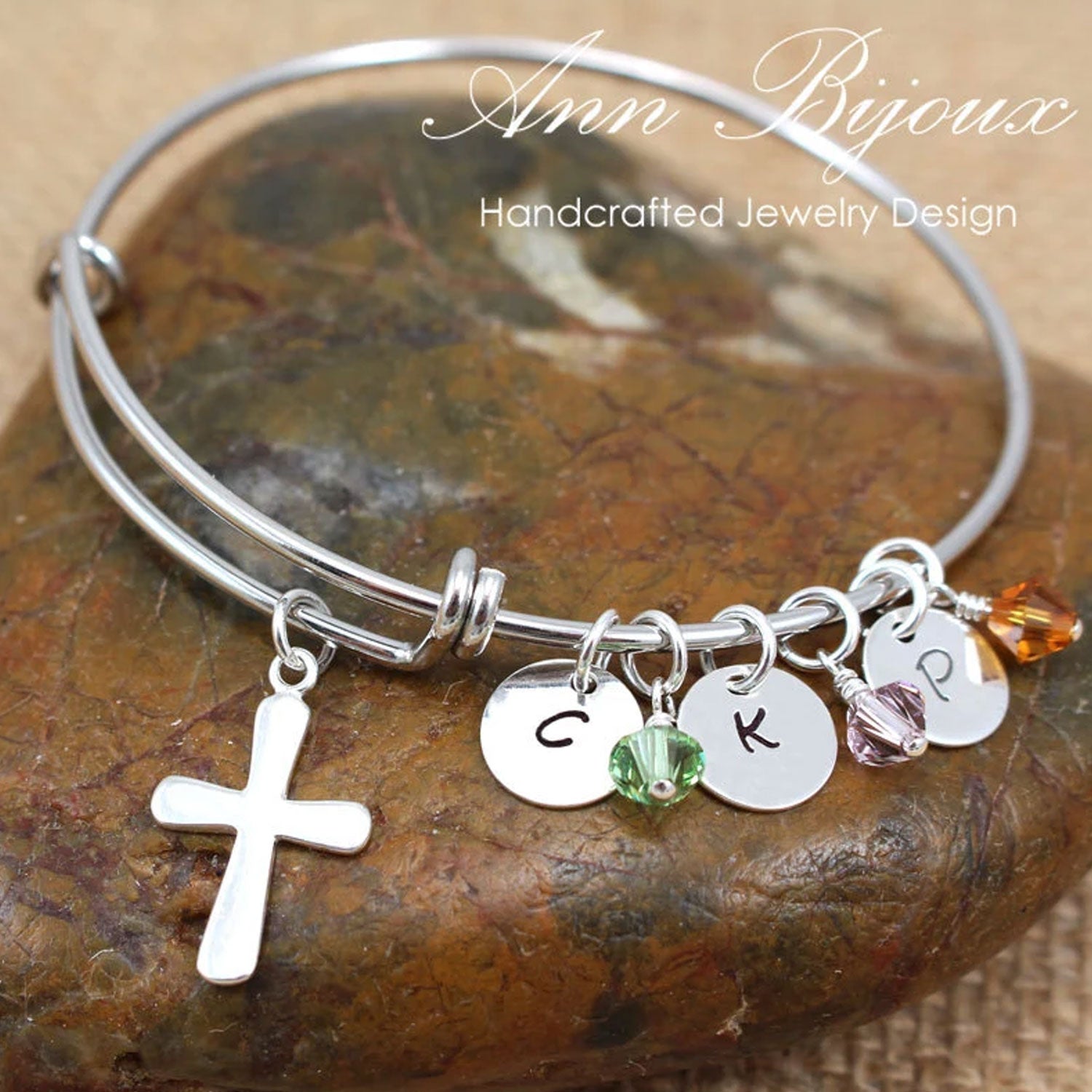 Silver bracelet with charms on a stone surface, featuring 'Ann Bijoux' branding.