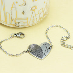 Silver bracelet with fingerprint heart charm on a yellow background