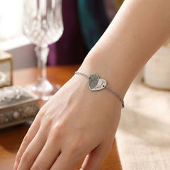 Silver bracelet with a heart-shaped charm on a wrist, blurred background