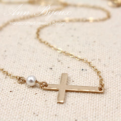 Gold sideways cross pendant with a hammered metal finish and a pearl bead detail. Personalized handcrafted jewelry on a gold chain, ideal for commemorative gifting.