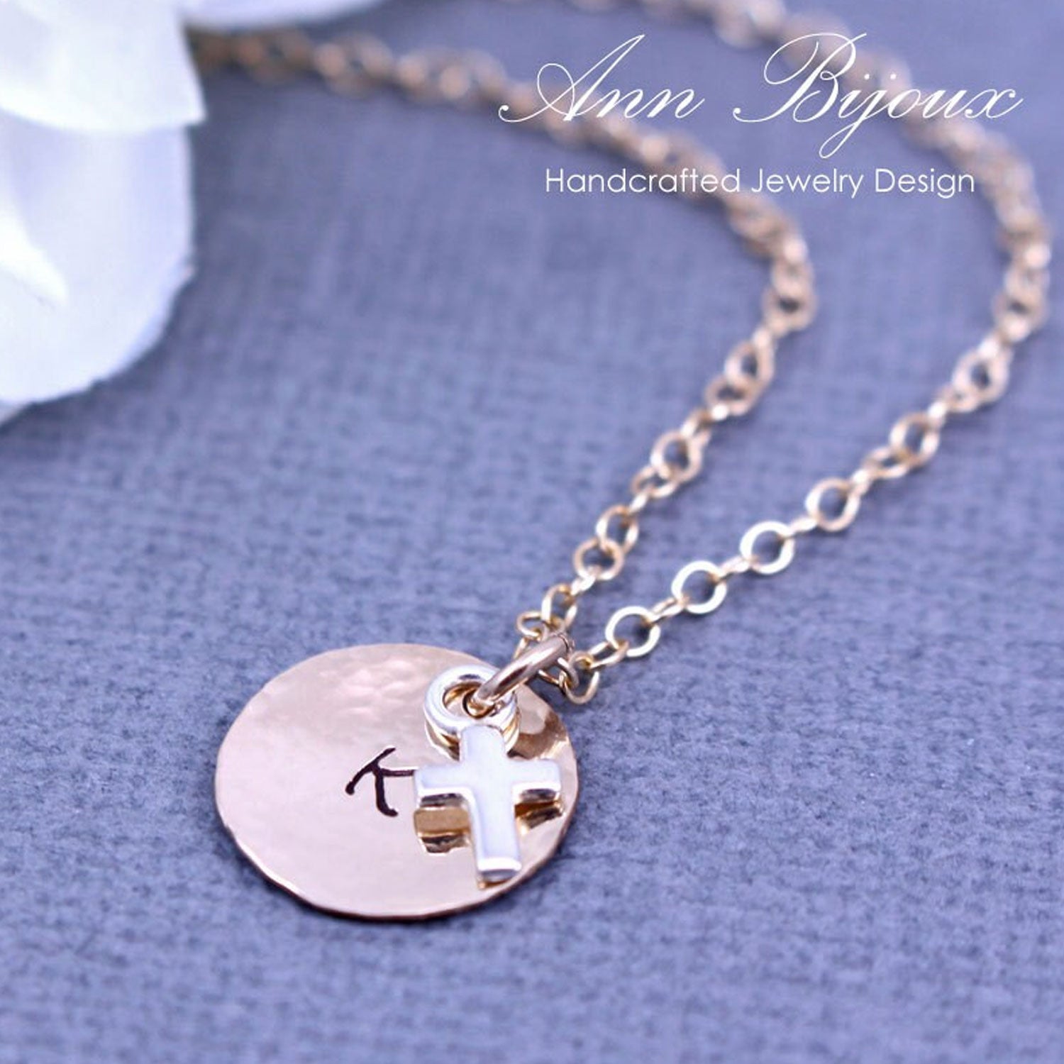 Gold necklace with a round pendant and cross charm on a gray background, branded 'Ann Bijoux'.