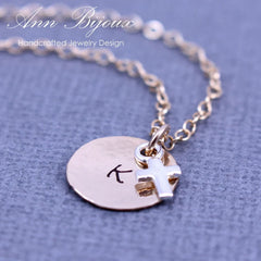 Necklace with round pendant and cross charm on a textured blue background, featuring 'Ann Bijoux' branding.