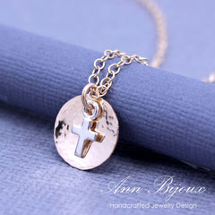 Necklace with a silver disc and cross pendant on a blue fabric background, featuring 'Ann Bijoux' branding.