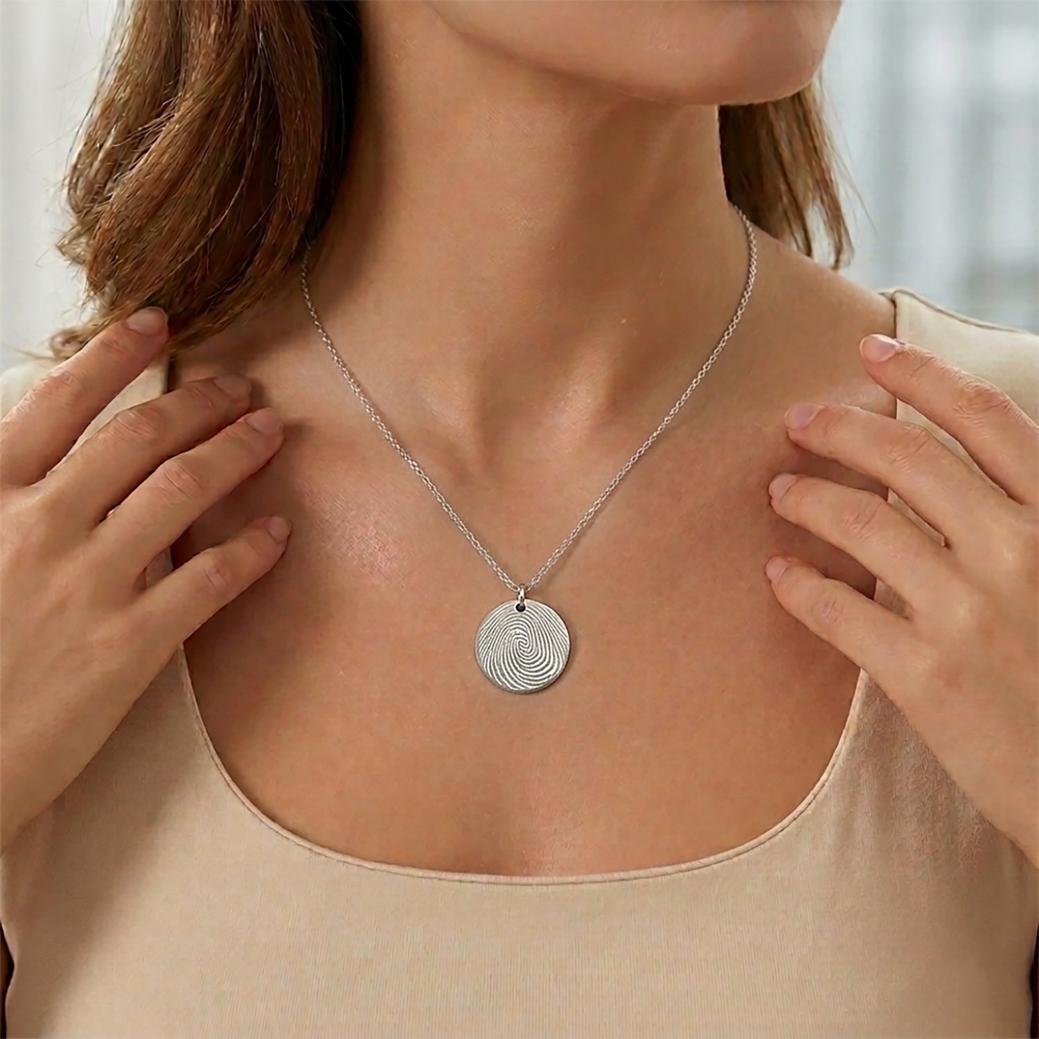 Person wearing a silver necklace with a circular pendant, hands adjusting the necklace.