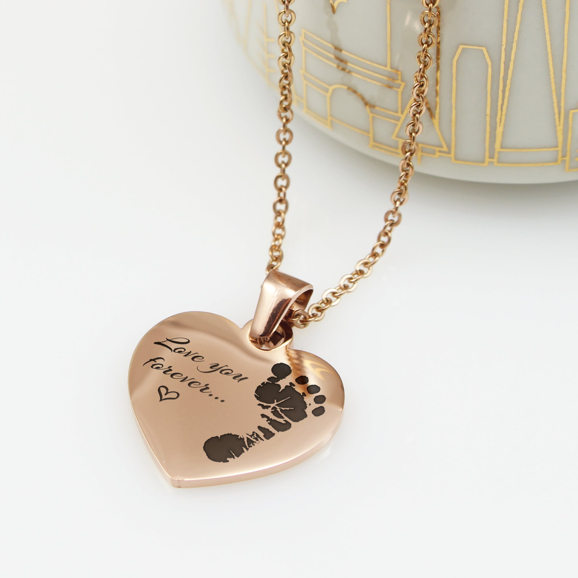 Heart-shaped pendant with engraved text and footprints on a white background